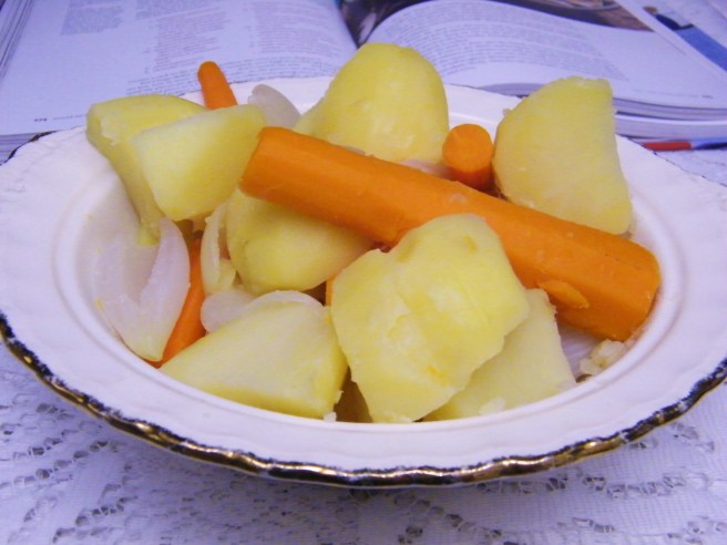 The cooked carrots, onions and potatoes arranged in a pretty dish, with a cookbook in the background.